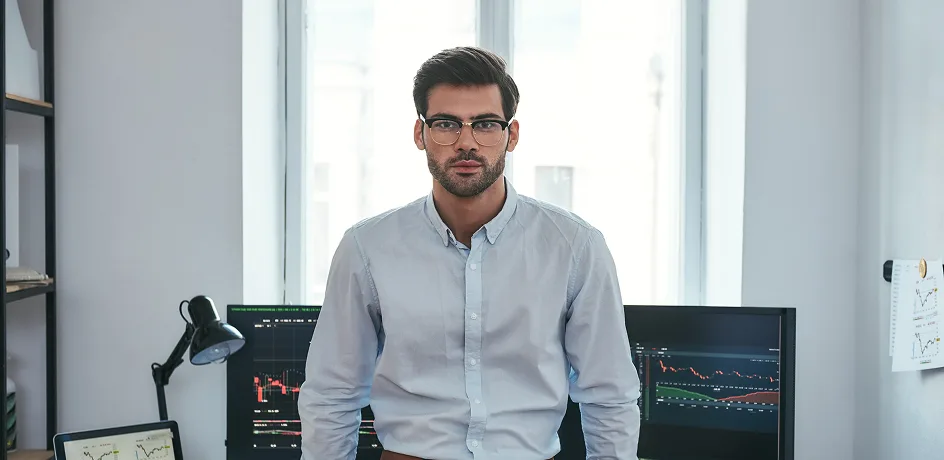 Data analyst standing in office with multiple financial and performance charts displayed on computer monitors